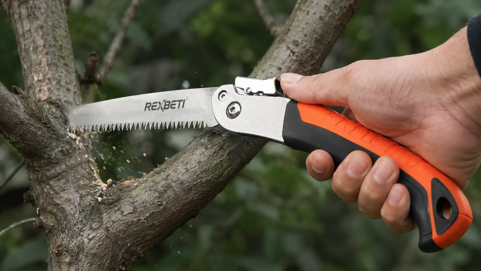 Hand gripping the REXBETI folding saw's handle mid-cut on a thick branch, blade teeth visible
