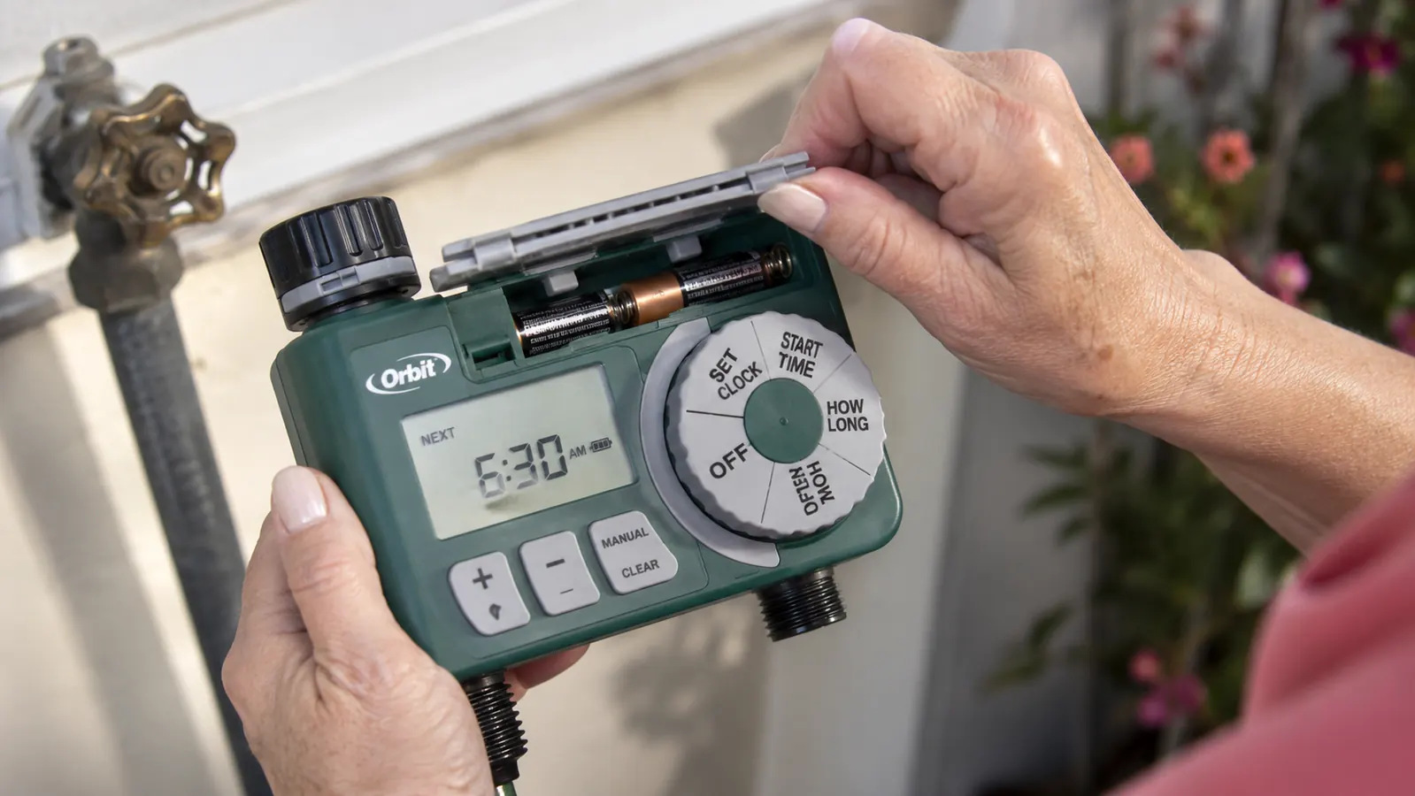 Hand lifting the battery door on the back of the Orbit timer to check the AA batteries