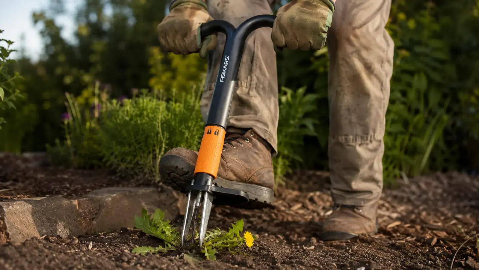 Hand and boot pressing down on the foot platform of the stand-up weed puller to drive the claws into the soil