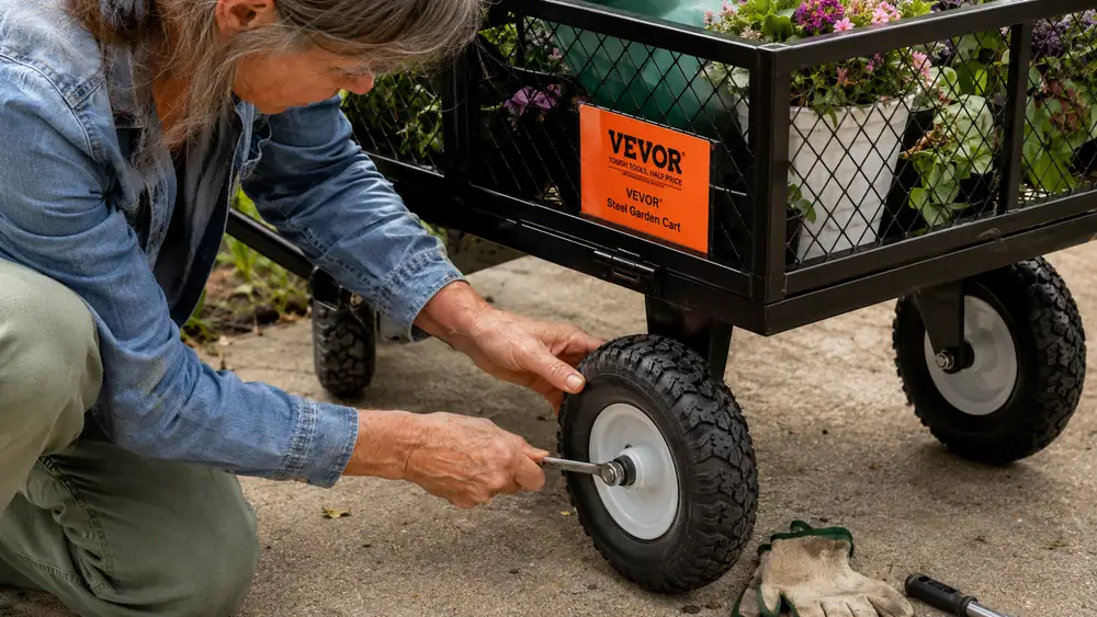 Hands using a wrench to check a wheel bolt on the steel garden cart's axle